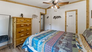 Un dormitorio con un aparador de madera, una cama con colcha estampada, un ventilador de techo y una puerta con la leyenda 'PRIVADO'.