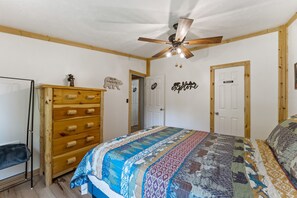 A bedroom with a wooden dresser, a bed with a colorful quilt, a ceiling fan, and a door labeled "PRIVATE".