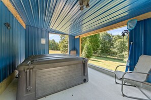 A hot tub in a covered outdoor area with a view of a grassy field and trees.