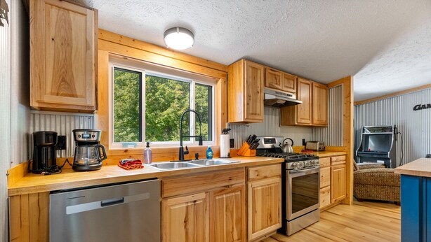 Una cocina moderna con armarios de madera, electrodomésticos de acero inoxidable y un amplio ventanal con vistas a zonas verdes.