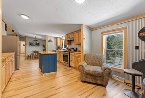A spacious kitchen with wooden cabinets, a central island, and a large window providing a view of the outdoors.