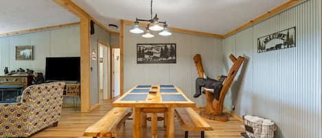 A wooden dining table with benches, a patterned sofa, a television, and a 'Welcome' sign on the wall.
