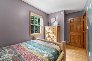 Un dormitorio con una cama de madera, una ventana, un aparador de madera y una puerta.