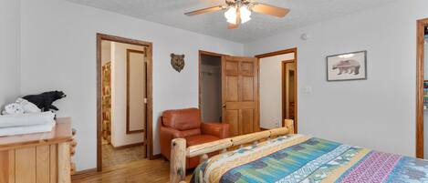 A bedroom with a wooden bed, a ceiling fan, a wooden wardrobe, and a brown leather chair.