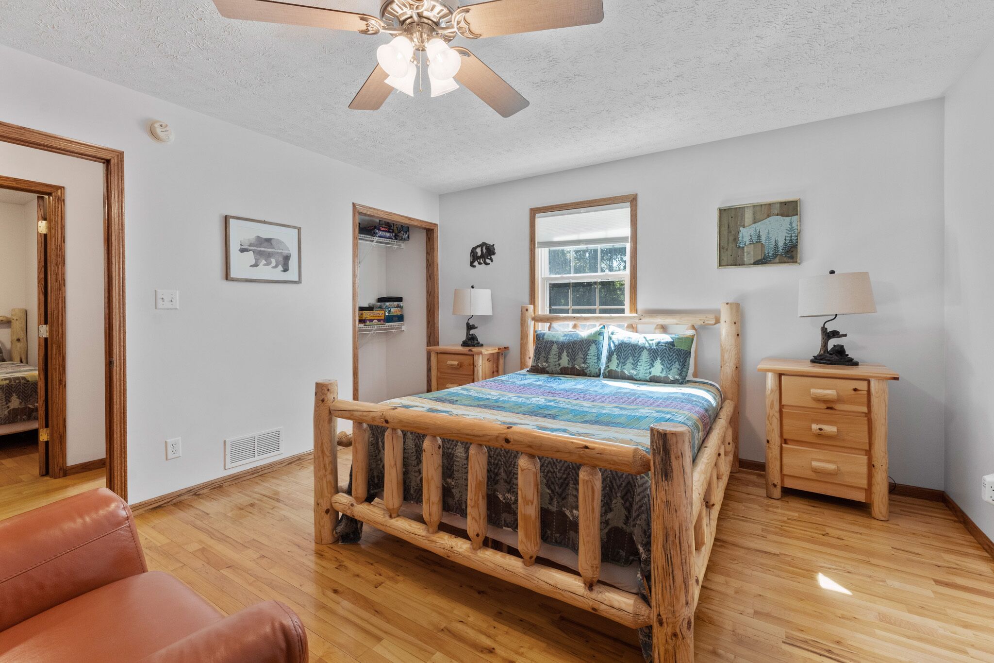 A bedroom with a wooden bed, a ceiling fan, a window, a bedside table with a lamp, and a mirror.