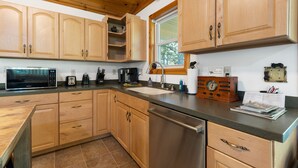 A kitchen with wooden cabinets, a stainless steel dishwasher, a microwave, a coffee maker, and a radio. - Bearadise Ridge | Hocking Hills, Game Room, Arcade (Laurelville)