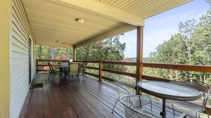 A covered outdoor deck with a wooden floor, metal chairs, a table, and a railing. - Bearadise Ridge | Hocking Hills, Game Room, Arcade (Laurelville)