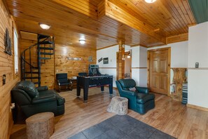 Un intérieur chaleureux avec des éléments en bois, notamment un baby-foot, des canapés en cuir, un escalier en colimaçon et un tronc d’arbre rustique.