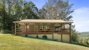 A rustic cabin with a wooden deck, a covered porch, and a fenced-in area with a bear enclosure. - Bearadise Ridge | Hocking Hills, Game Room, Arcade (Laurelville)