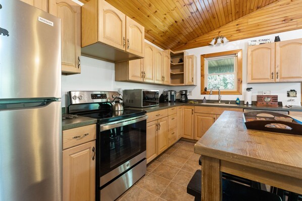 A modern kitchen with stainless steel appliances, wooden cabinets, and a wooden ceiling.