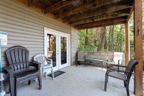 A covered patio with outdoor seating, including chairs and a bench, and a door leading to a building.