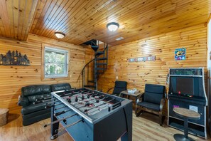 A wooden-floored room with a foosball table, a sofa, a chair, and a small table with a game console.