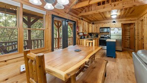 A wooden cabin interior with a dining table, benches, a kitchen area, and large windows. - Beartastic Outlook | Hocking Hills, Hot Tub (Rockbridge)