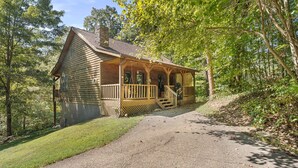 A wooden cabin with a porch and steps leading to the entrance, surrounded by trees and a gravel path. - Beartastic Outlook | Hocking Hills, Hot Tub (Rockbridge)