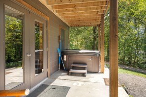 A covered outdoor area with a hot tub, a door, and a step leading to a covered entrance. - Beartastic Outlook | Hocking Hills, Hot Tub (Rockbridge)