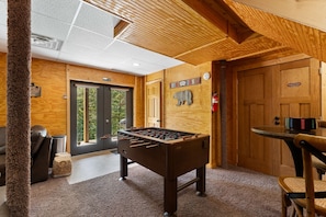 A cozy indoor space with a foosball table, a wooden wall with a bear decoration, and a door labeled "Calgary". - Beartastic Outlook | Hocking Hills, Hot Tub (Rockbridge)