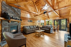 A cozy cabin interior with a stone fireplace, wooden beams, leather sofas, and a dining area. - Beartastic Outlook | Hocking Hills, Hot Tub (Rockbridge)