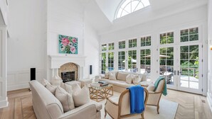 A spacious living room with a fireplace, large windows, and a view of the outdoors. - Spacious & chic Southampton estate with heated pool, fire pit &... (Southampton)