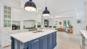 A spacious kitchen with white cabinetry, a large island, and two pendant lights. - Spacious & chic Southampton estate with heated pool, fire pit &... (Southampton)