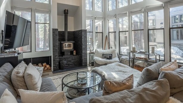 A spacious living room with a stone fireplace, large windows, and a cozy seating area. - Bright, beautiful condo in the heart of Mammoth, near shuttle, shops, ski & golf (Mammoth Lakes)