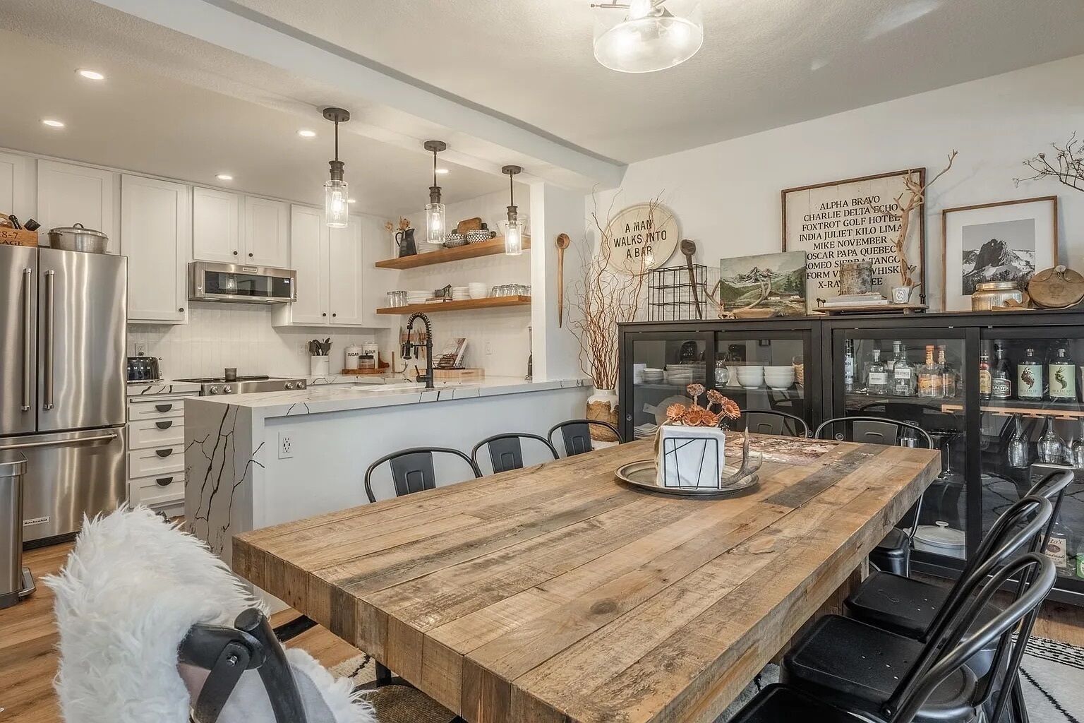 A modern kitchen with white cabinets, a wooden dining table, and a bar area with liquor bottles.
