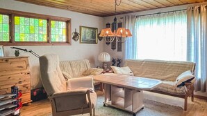 A cozy living room with a sofa, armchair, and a coffee table. There are windows with curtains, a chandelier, and a wooden dresser. - 4 Person Holiday Home in Smedstorp (Tomelilla)