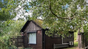 A rustic cabin with a large window, surrounded by lush greenery and a wooden fence. - 4 Person Holiday Home in Smedstorp (Tomelilla)