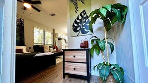 Un saló modern amb un sofà negre, un paviment de fusta, un ventilador de sostre i una gran planta amb fulles.