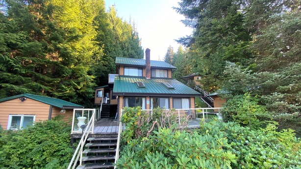 Une maison à deux étages, dotée d’un toit végétalisé et entourée d’une forêt dense.