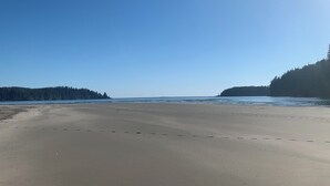Une vaste plage de sable fin, avec des eaux calmes et des îles boisées à l’horizon.