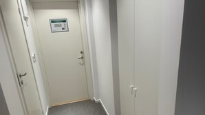 A narrow hallway with white walls and a tiled floor. There is a door at the end with a sign above it. - Apartment 21 in Sollentuna Stockholm (Sollentuna)