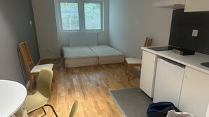 A compact room with a sofa bed, a small dining table with chairs, a kitchenette, and a window with blinds. - Apartment 21 in Sollentuna Stockholm (Sollentuna)