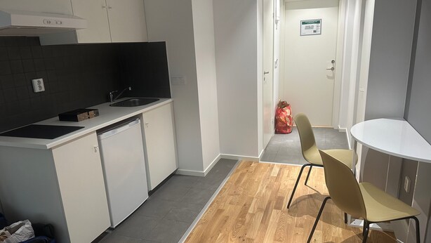 A modern kitchen with white cabinets, a black countertop, and a wooden floor. There is a small dining area with a table and two chairs. - Apartment 21 in Sollentuna Stockholm (Sollentuna)