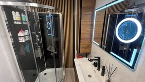 A modern bathroom with a glass-enclosed shower, a vanity with a mirror, and toiletries on shelves. - Lake - Golden Triangle (Annecy)