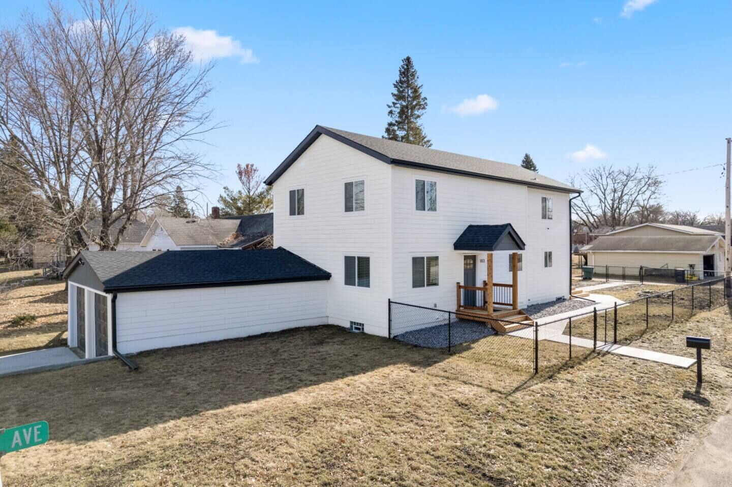 Une maison à deux étages avec un garage, une cour clôturée et un petit porche.