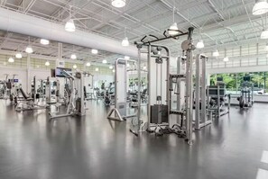 Une salle de sport spacieuse, dotée de divers appareils d’entraînement, de grandes fenêtres et d’un plafond haut.