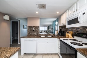 A modern kitchen with white cabinets, a granite countertop, a built-in microwave, and a stove.