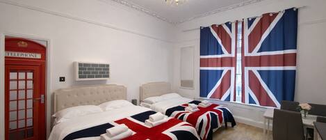 A hotel room with two beds, a telephone, a chandelier, and a large window with a Union Jack curtain.
