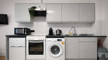 Eine kompakte Küche mit Mikrowelle, Backofen, Waschmaschine und einem kleinen Spülbecken.