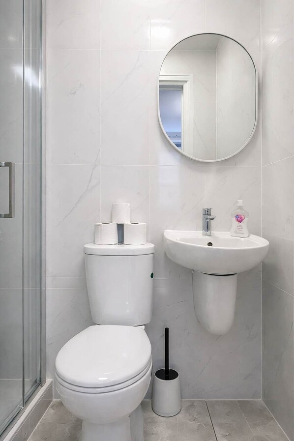 Un baño con inodoro, lavamanos, espejo y zona de ducha.