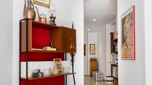 Un corridoio con una libreria in legno, uno scaffale imbottito rosso e una lampada vintage.