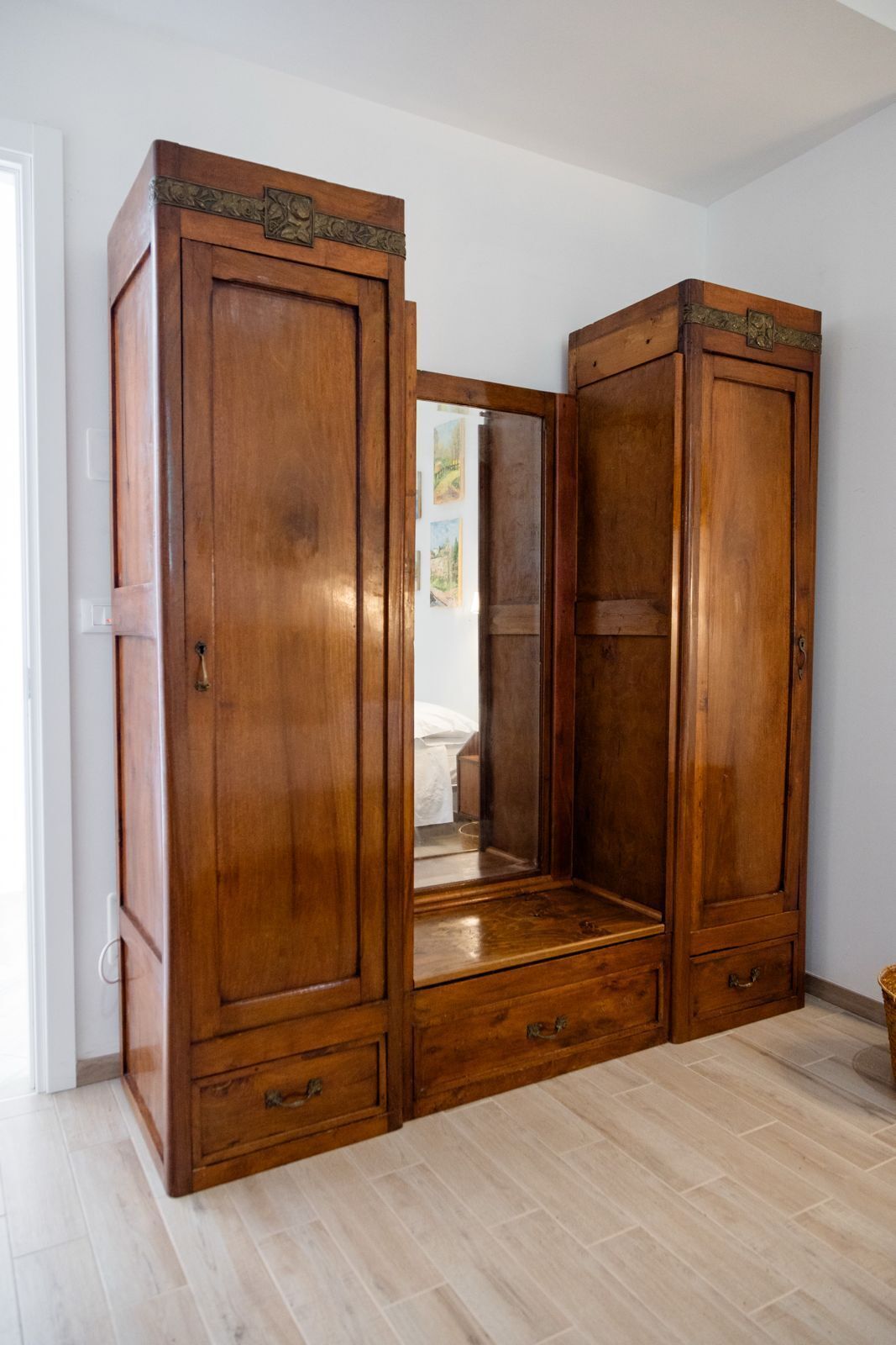 Une armoire en bois avec un miroir et deux tiroirs, située dans une pièce dont le plancher est recouvert de bois de couleur claire.