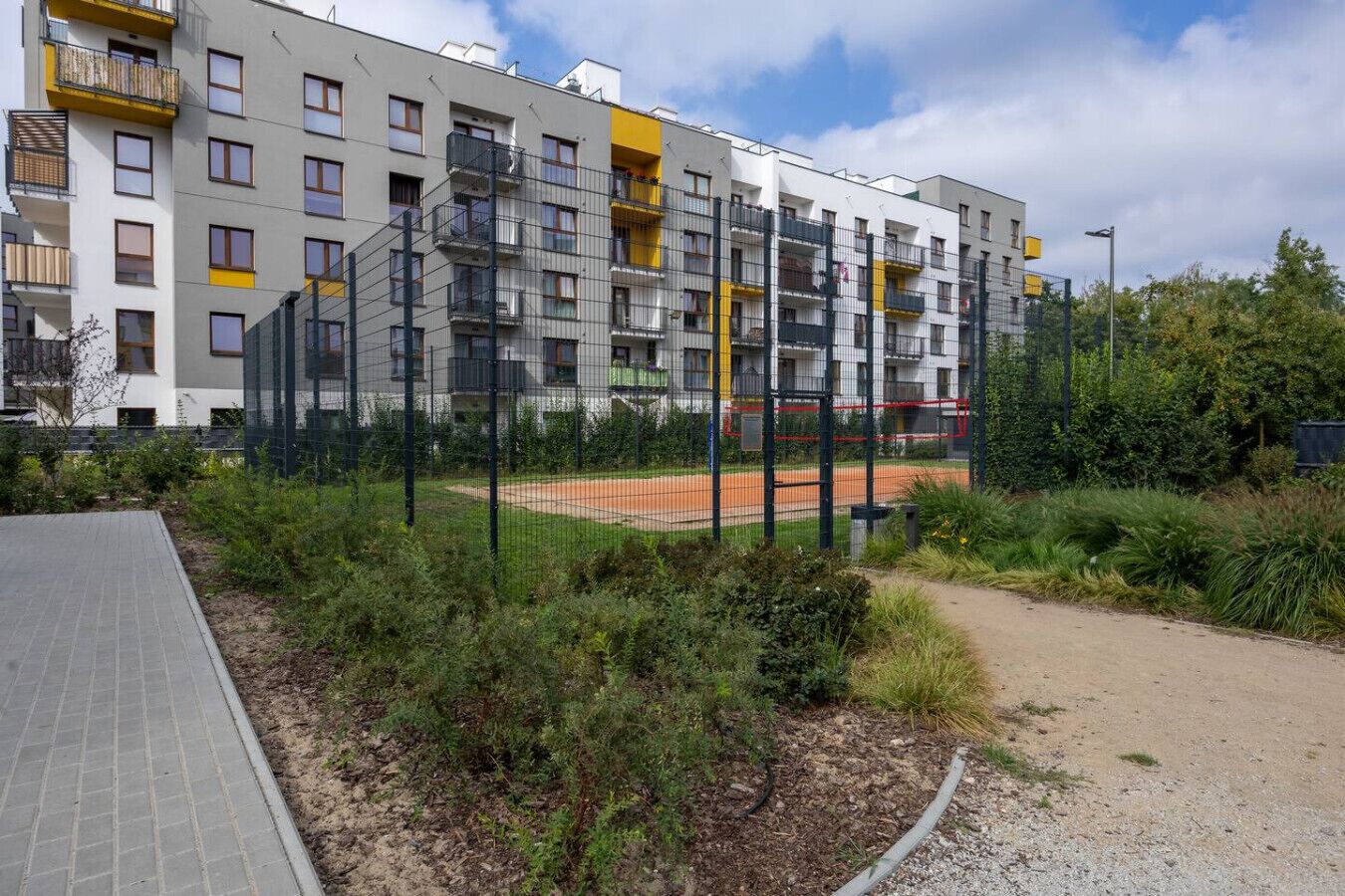 Un immeuble d’appartements moderne doté de nombreux balcons, d’un terrain de sport et d’un chemin pavé.