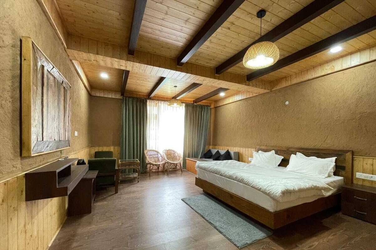 A bedroom with a wooden ceiling, a large bed, a desk, and two chairs.
