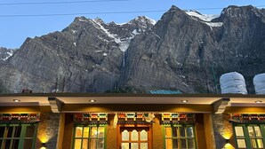 Un edificio con puerta de madera, ventanas con marco verde y fachada de piedra, con vistas a montañas nevadas al fondo.