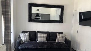 Ett modernt vardagsrum med en svart lädersoffa, en stor spegel och en hänglampa.