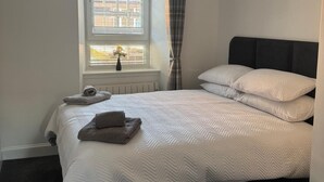 Ett sovrum med en säng, ett fönster med persienner, ett element, en hängande lampa och en gardin.