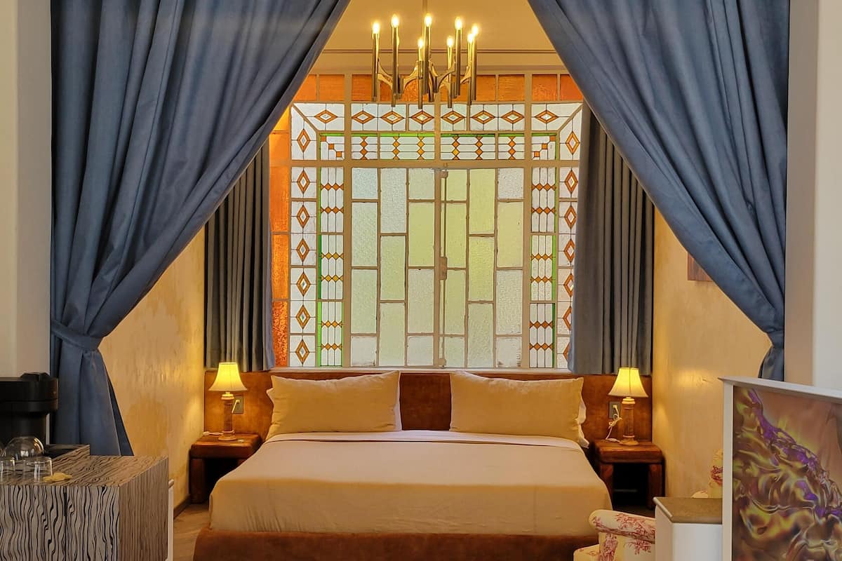 A bedroom with a large bed, two bedside tables with lamps, a decorative wall panel, and a painting on the wall.