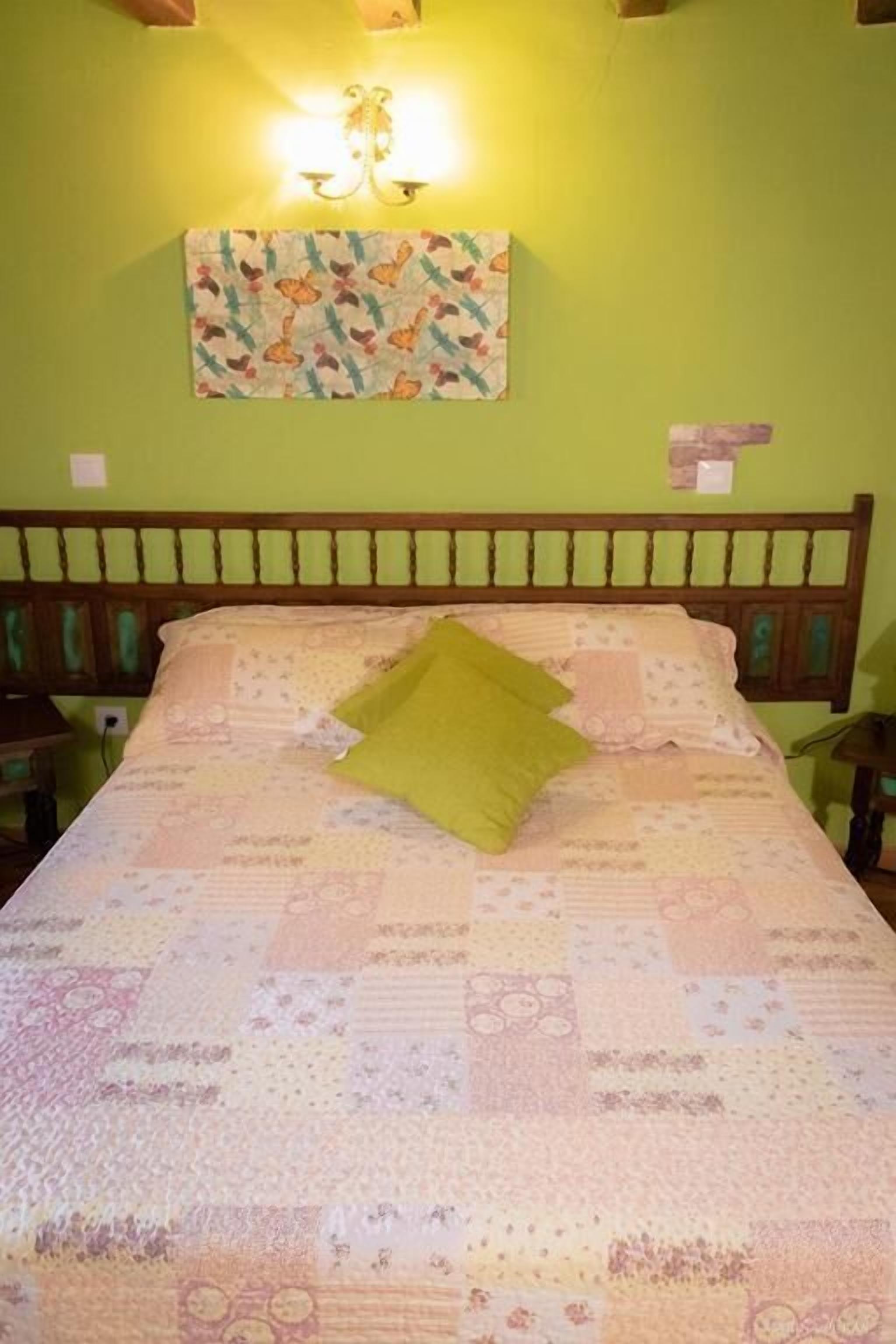 A bed with a quilt, a green pillow, and a wall-mounted light fixture.