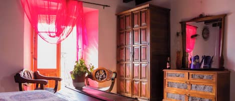 A bedroom with a bed, a wooden cabinet, a chair, and a table with a plant.